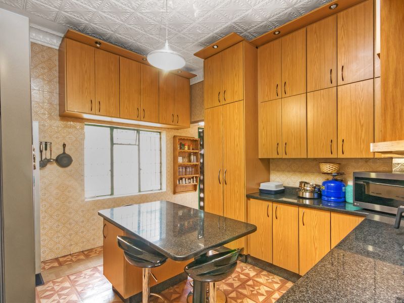 A functional kitchen featuring extensive wooden cabinetry, granite countertops, a built-in breakfast island, and a distinctive pressed metal ceiling.