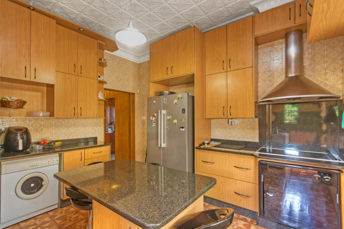 A functional kitchen featuring extensive wooden cabinetry, granite countertops, a built-in oven with extractor fan, and integrated laundry facilities.