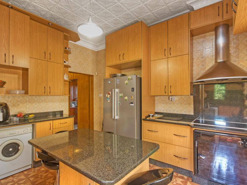 A functional kitchen featuring extensive wooden cabinetry, granite countertops, a built-in oven with extractor fan, and integrated laundry facilities.
