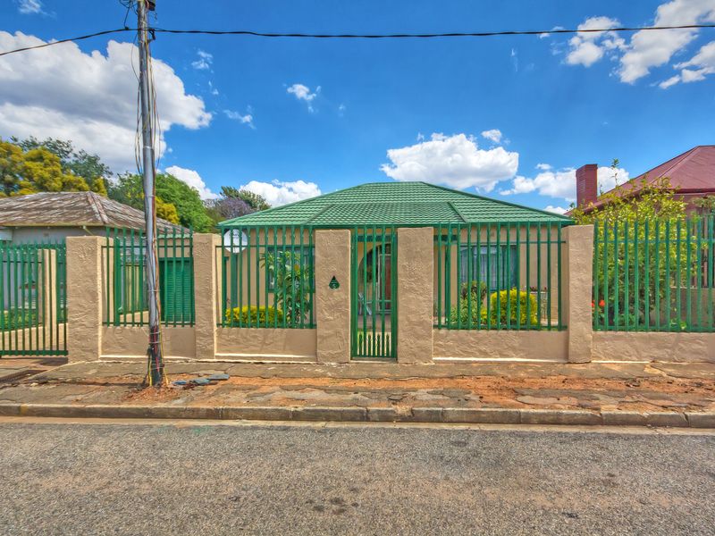 Front elevation of a residential property featuring a green tiled roof, secure perimeter wall with metal fencing, and a gated pedestrian entrance.