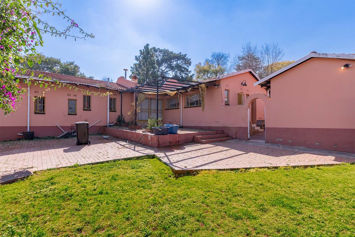 Rear exterior view of the house featuring a paved patio area, a pergola structure, and a garden space with established brick walling.