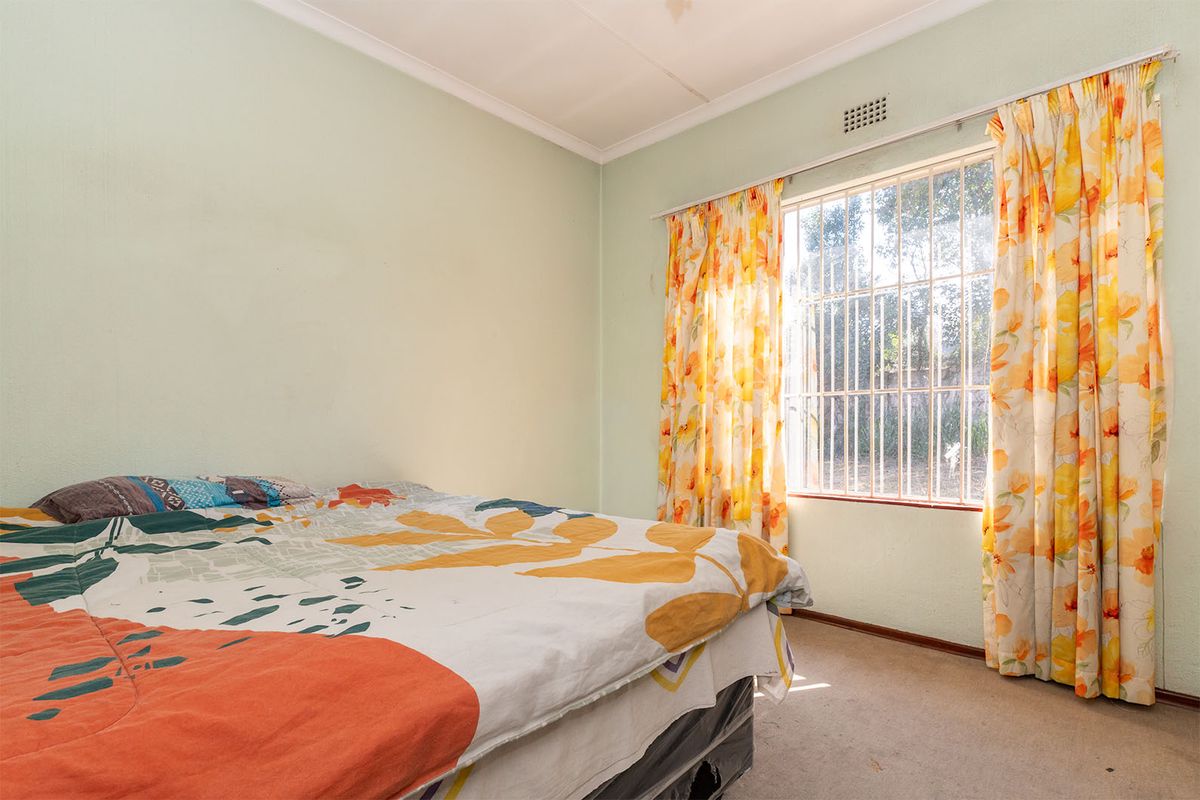 A bedroom featuring a window with security bars, cornice detailing, and ventilation, requiring cosmetic updates to the flooring and wall finishes.