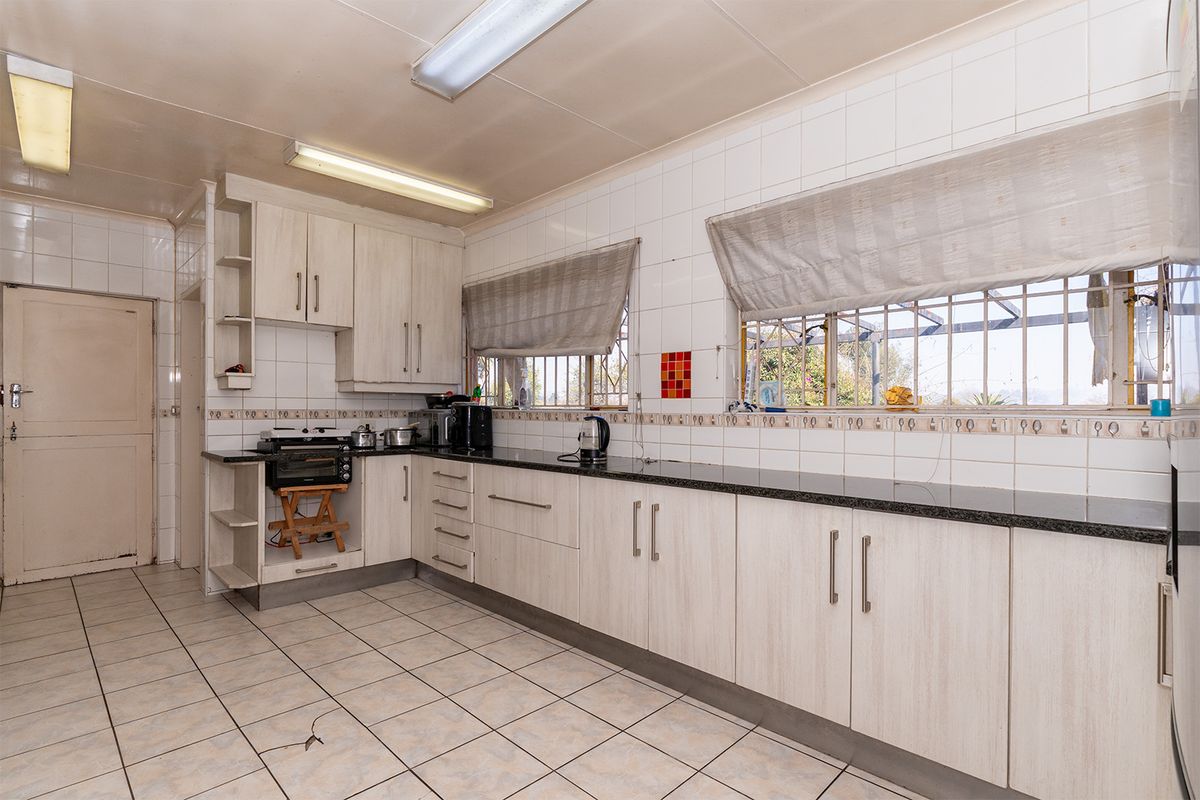 A functional kitchen featuring light-toned built-in cabinetry, granite countertops, ceramic tile backsplash, and tiled flooring with security bars on the windows.