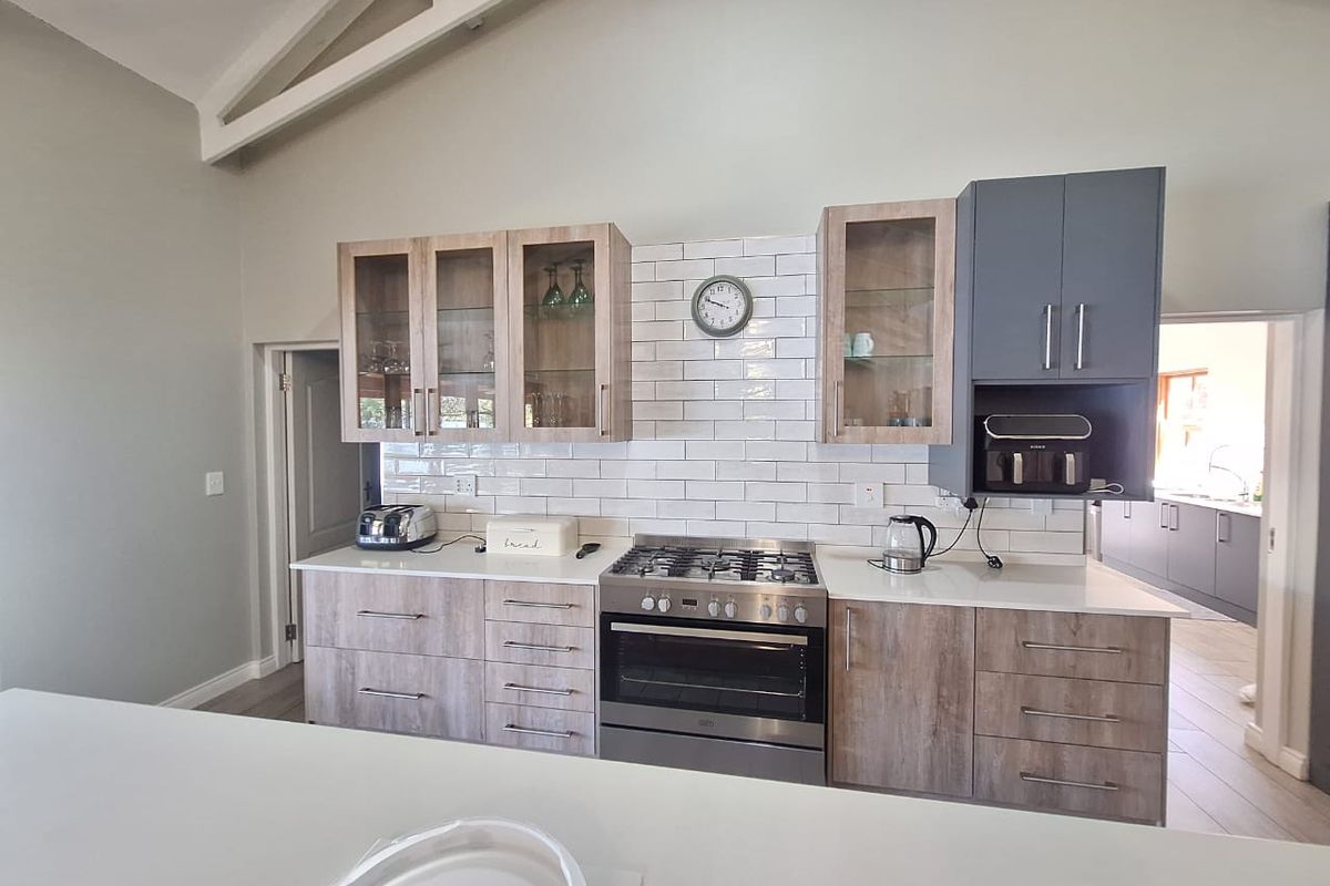 Modern kitchen featuring light wood-tone cabinetry, contrasting grey upper cabinets, white subway tile backsplash, gas hob, and a spacious vaulted ceiling.