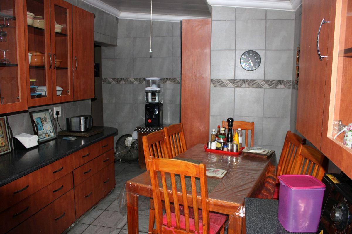 A functional kitchen featuring wooden cabinetry, dark countertops, and full-height wall tiling, providing a practical workspace with an integrated dining area.