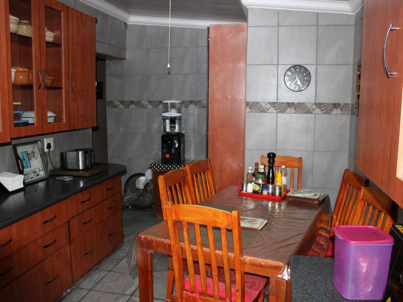 A functional kitchen featuring wooden cabinetry, dark countertops, and full-height wall tiling, providing a practical workspace with an integrated dining area.