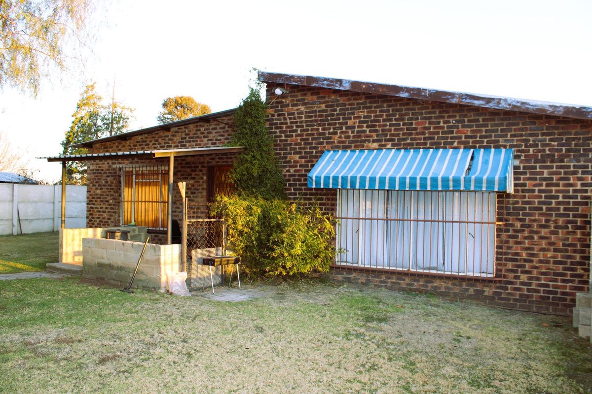 Rear view of a face brick small holding dwelling featuring a small patio area, metal security bars, and a striped window awning.