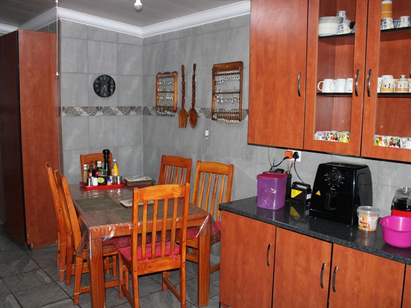 A functional kitchen area featuring wooden cabinetry, granite countertops, and full-height wall tiling, providing a practical space for meal preparation and dining.