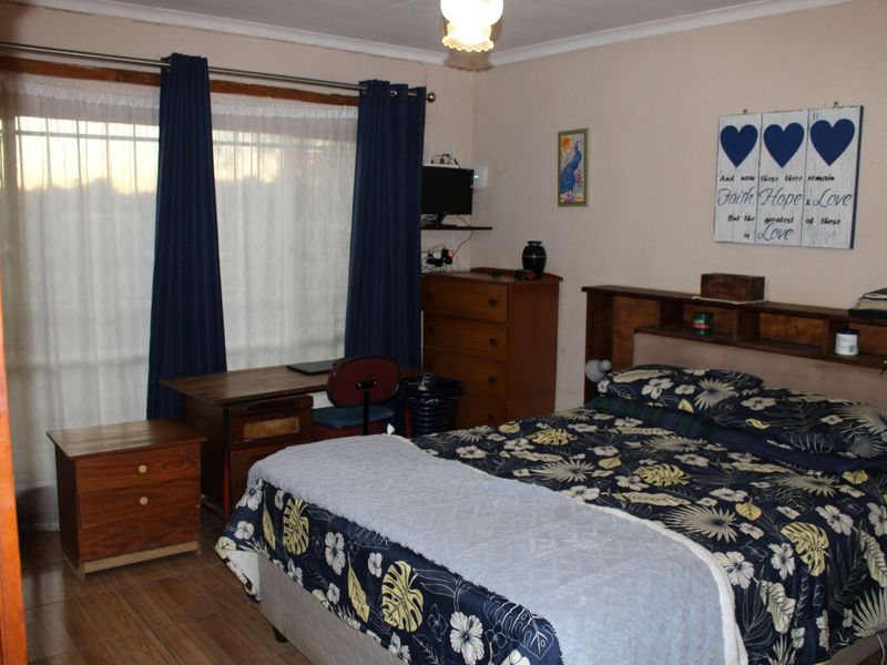 A functional bedroom featuring tiled flooring, a built-in headboard, and a large window fitted with security bars.