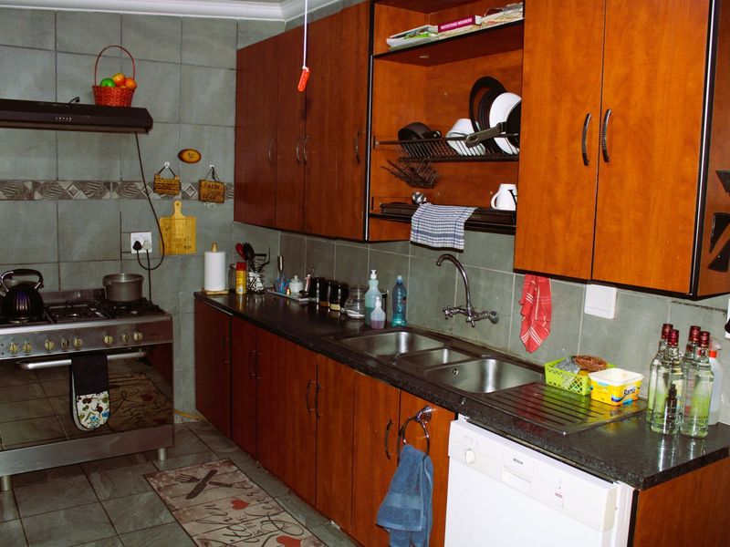 A functional kitchen featuring wooden cabinetry, granite countertops, a double stainless steel sink, and a gas stove with an extractor fan.