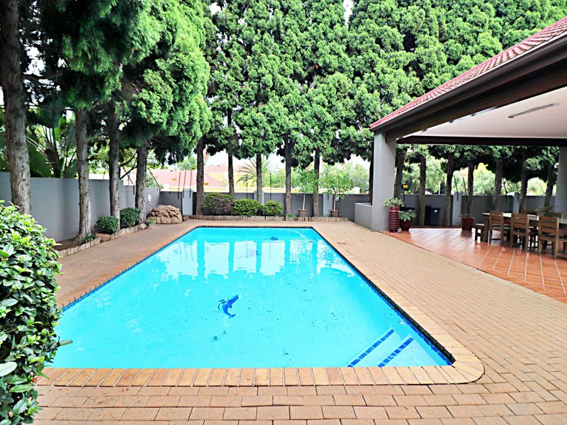 Outdoor swimming pool area featuring brick paving, a covered patio space, and established perimeter trees providing privacy.
