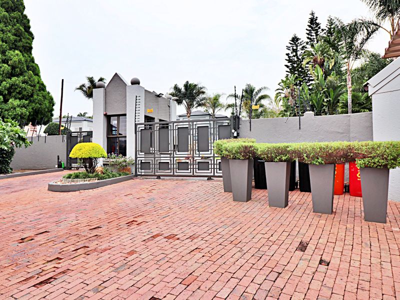 Front entrance area of the apartment complex featuring a brick paved driveway, secure gated access, and a guard house with perimeter security fencing.
