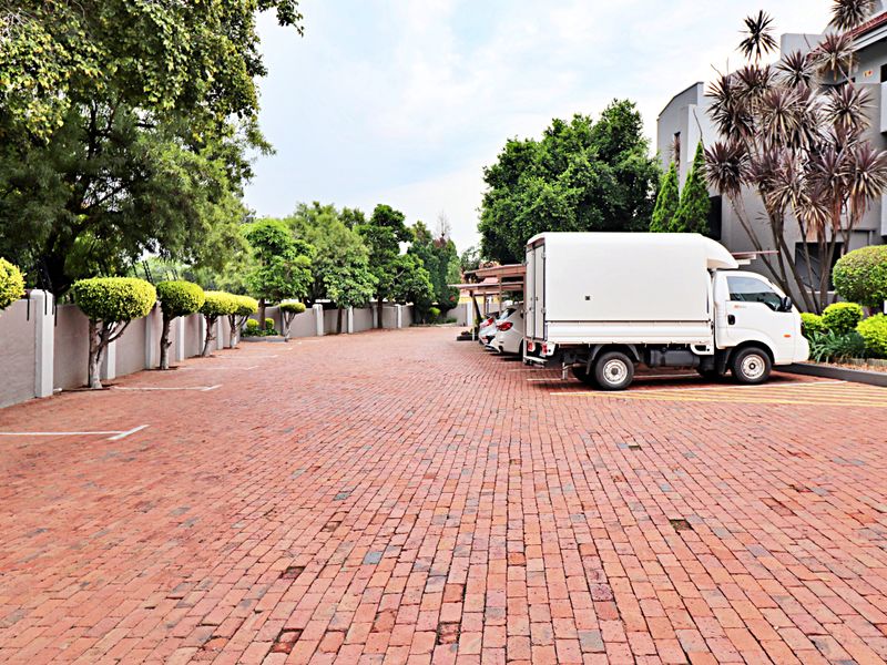 A paved parking area for the apartment complex featuring perimeter walls, mature trees, and covered parking bays.