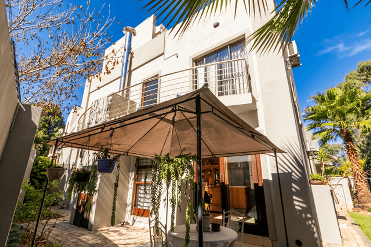 Rear elevation of the townhouse featuring a paved patio area, a first-floor balcony with stainless steel balustrades, and a prominent external flue pipe.