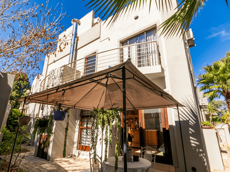 Rear elevation of the townhouse featuring a paved patio area, a first-floor balcony with stainless steel balustrades, and a prominent external flue pipe.