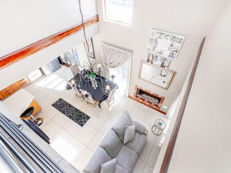 Spacious open-plan living and dining area featuring double volume ceilings, tiled flooring, and a built-in fireplace with direct access to the patio.