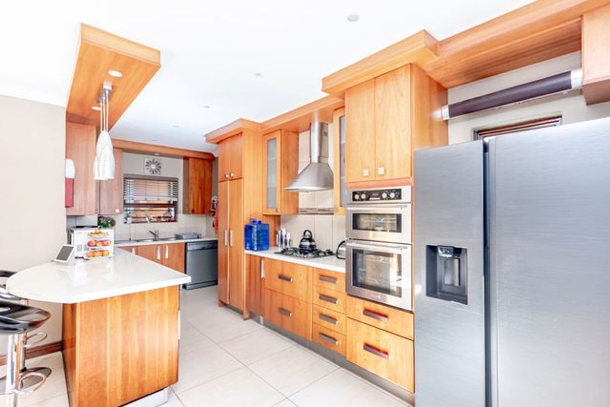 A well-appointed kitchen featuring warm wooden cabinetry, stone countertops, a breakfast bar, and integrated stainless steel appliances including a double oven and gas hob.