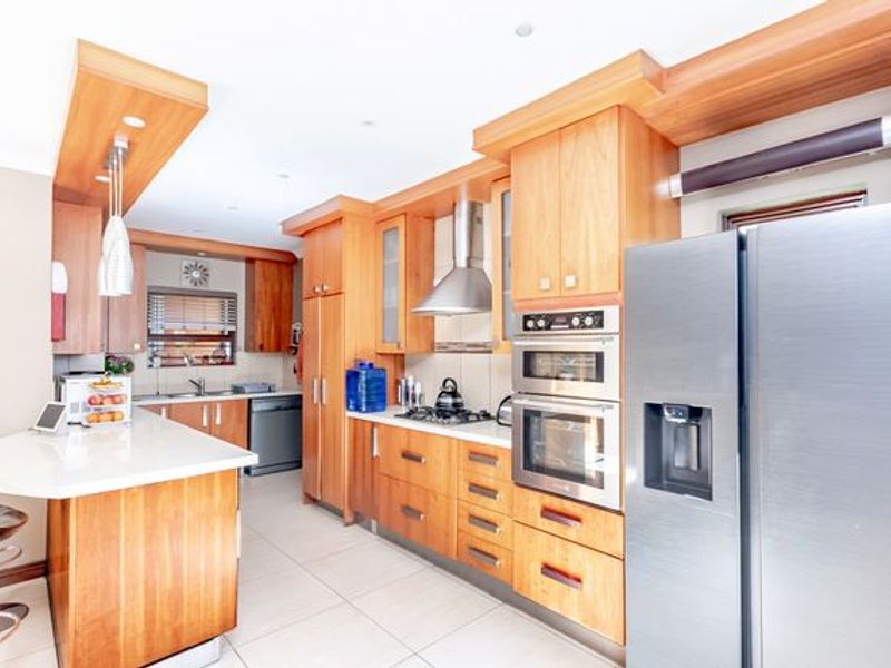 A well-appointed kitchen featuring warm wooden cabinetry, stone countertops, a breakfast bar, and integrated stainless steel appliances including a double oven and gas hob.