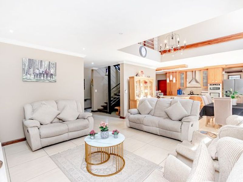 Spacious open-plan living area featuring tiled floors, a modern kitchen with built-in appliances, and a staircase leading to an upper level.