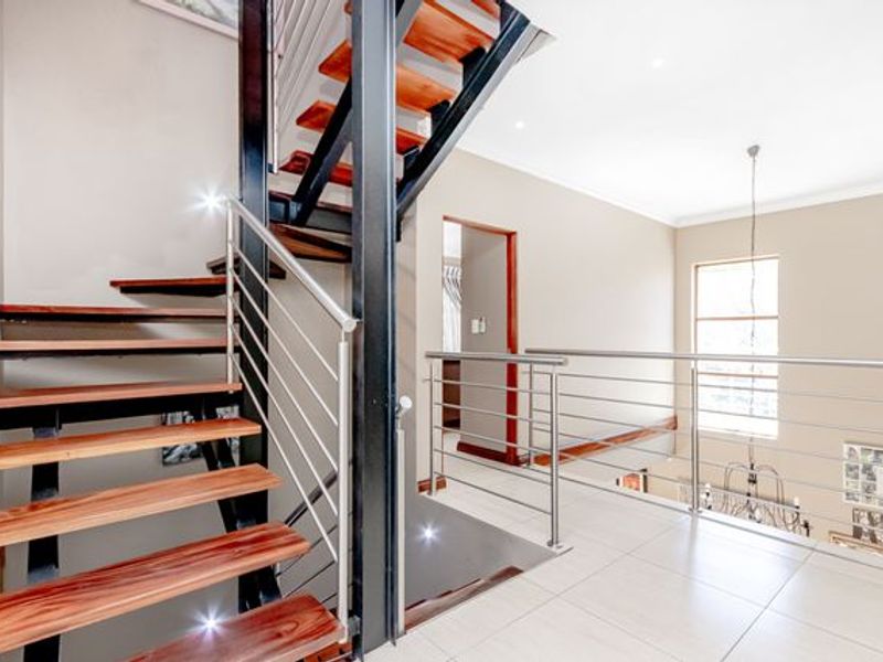 A bright landing area featuring a modern open-tread staircase with wooden steps, steel frame, and stainless steel balustrades, complemented by neutral tiled flooring.