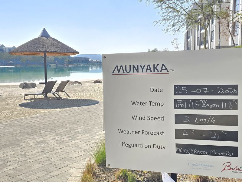 A view of the Munyaka estate pool area featuring a paved walkway, landscaped garden, and a clear swimming lagoon with beach-style surroundings.