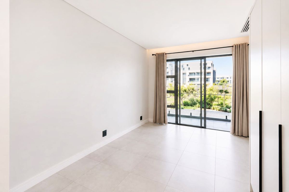 A bright, modern, and empty bedroom featuring large sliding glass doors leading to a balcony, neutral tiled floors, and built-in storage cabinetry.