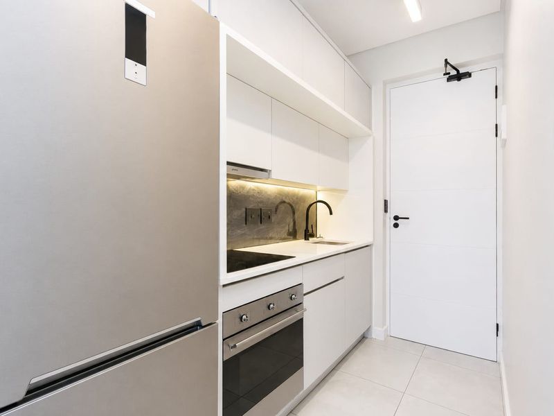 Modern, compact kitchen featuring sleek white cabinetry, integrated appliances, stone countertops, and high-quality matte black fixtures.