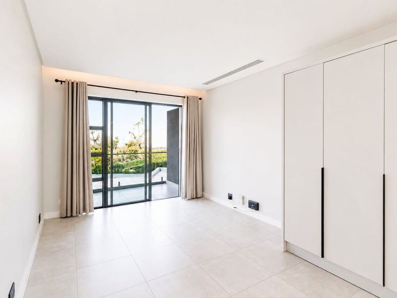 A bright, modern bedroom featuring neutral tiled floors, built-in wardrobes, and large sliding glass doors that open to a private balcony.
