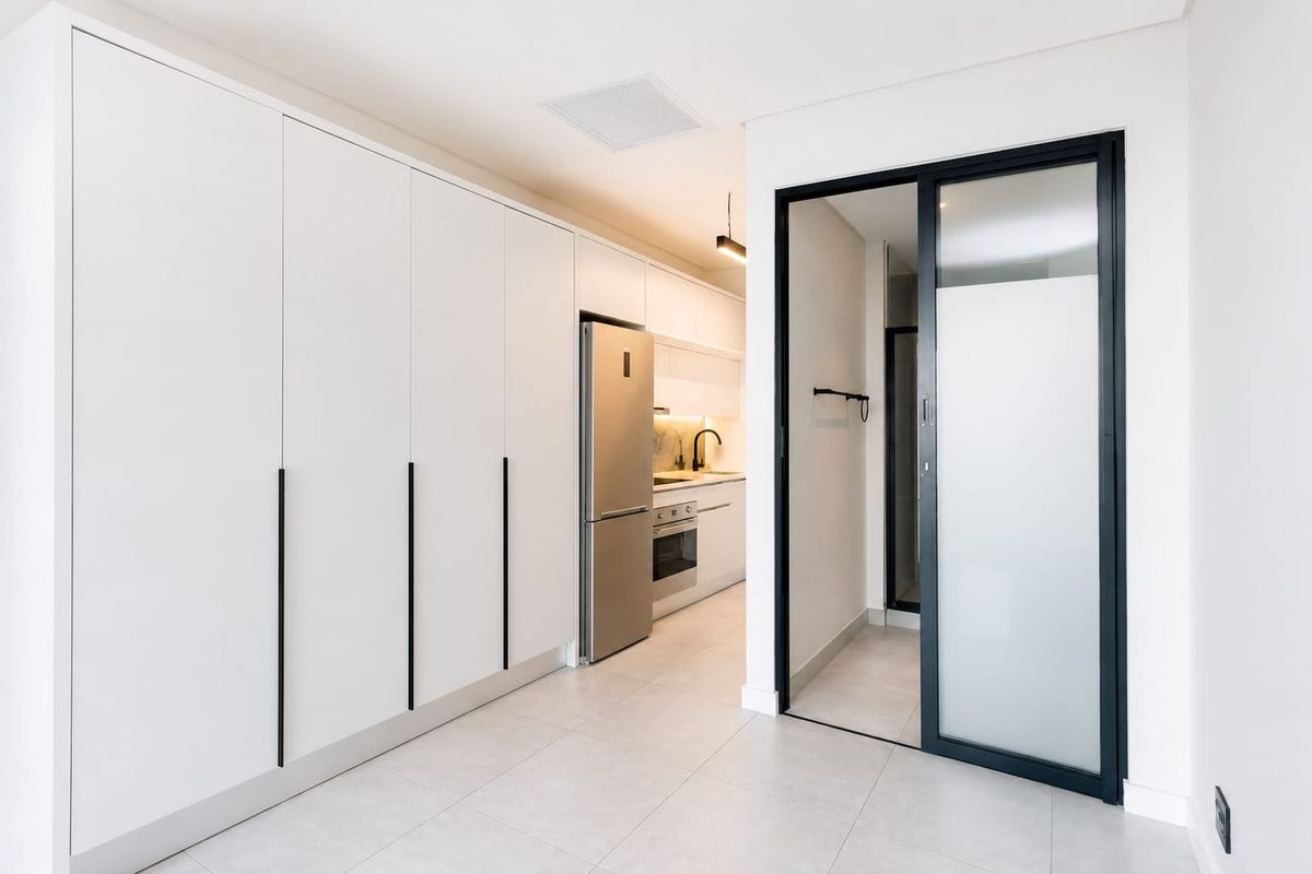 Modern kitchen featuring sleek white cabinetry, integrated appliances, tiled flooring, and a contemporary sliding glass door leading to an adjacent space.