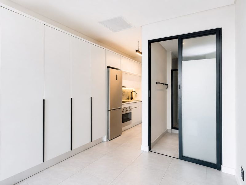 Modern kitchen featuring sleek white cabinetry, integrated appliances, tiled flooring, and a contemporary sliding glass door leading to an adjacent space.
