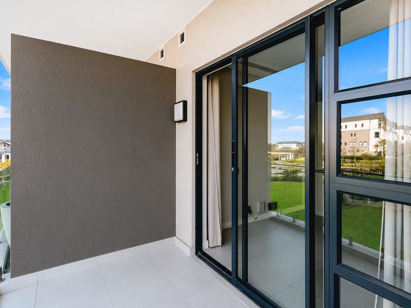 A modern, covered balcony featuring tiled flooring, a sleek glass balustrade, and large sliding glass doors providing access to the interior living space.
