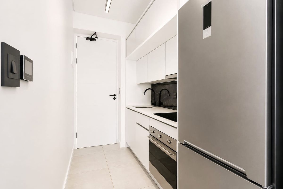 Modern galley-style kitchen featuring sleek white cabinetry, stone countertops, integrated appliances, and high-quality black fixtures in a clean, minimalist design.