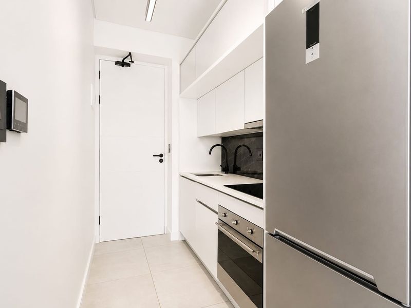 Modern galley-style kitchen featuring sleek white cabinetry, stone countertops, integrated appliances, and high-quality black fixtures in a clean, minimalist design.