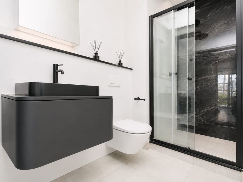 Modern bathroom featuring a wall-mounted vanity with a black vessel sink, wall-hung toilet, and a sleek walk-in shower with black frame detailing.