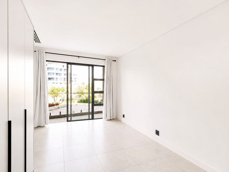 Bright and modern bedroom featuring neutral tiled flooring, built-in cupboards, and a sliding glass door leading to an outdoor balcony area.