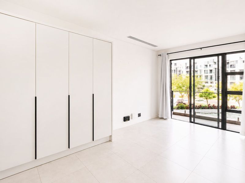 Bright and modern bedroom featuring built-in cupboards, tiled flooring, and large sliding glass doors leading to a private balcony.
