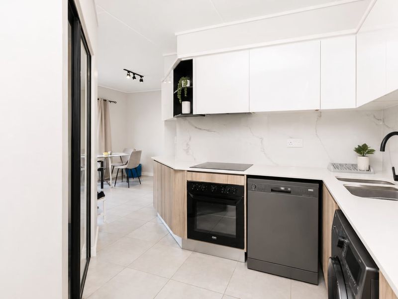 Modern kitchen featuring sleek white and wood-tone cabinetry, marble-look splashback, integrated appliances, and high-quality matte black fixtures in an open-plan layout.