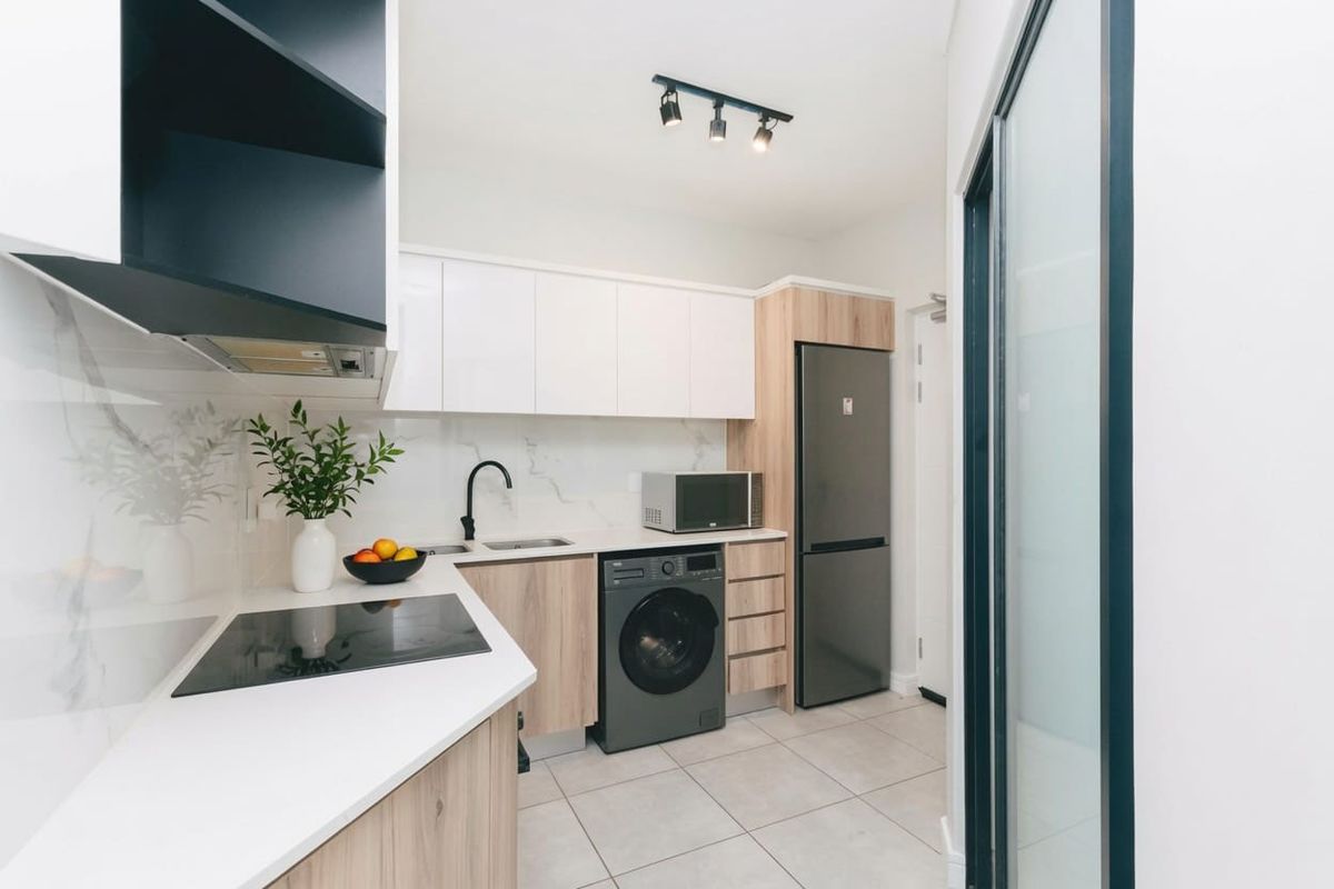 Modern, compact kitchen featuring sleek white and wood-grain cabinetry, stone countertops, integrated appliances, and contemporary track lighting.