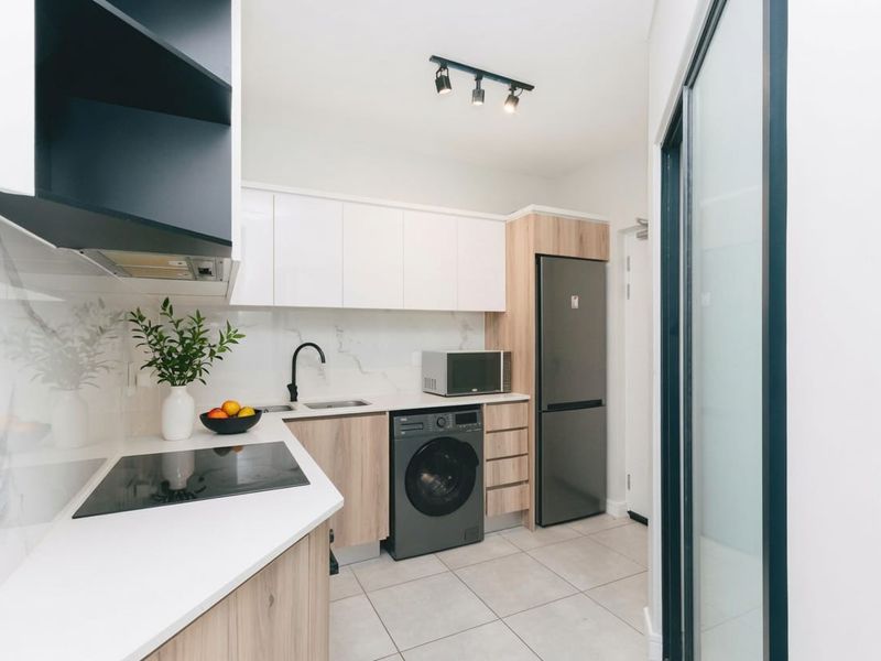 Modern, compact kitchen featuring sleek white and wood-grain cabinetry, stone countertops, integrated appliances, and contemporary track lighting.
