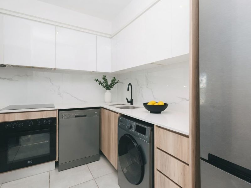 Modern kitchen featuring sleek white cabinetry, marble-look splashback, built-in oven, hob, and integrated laundry and dishwasher appliances.
