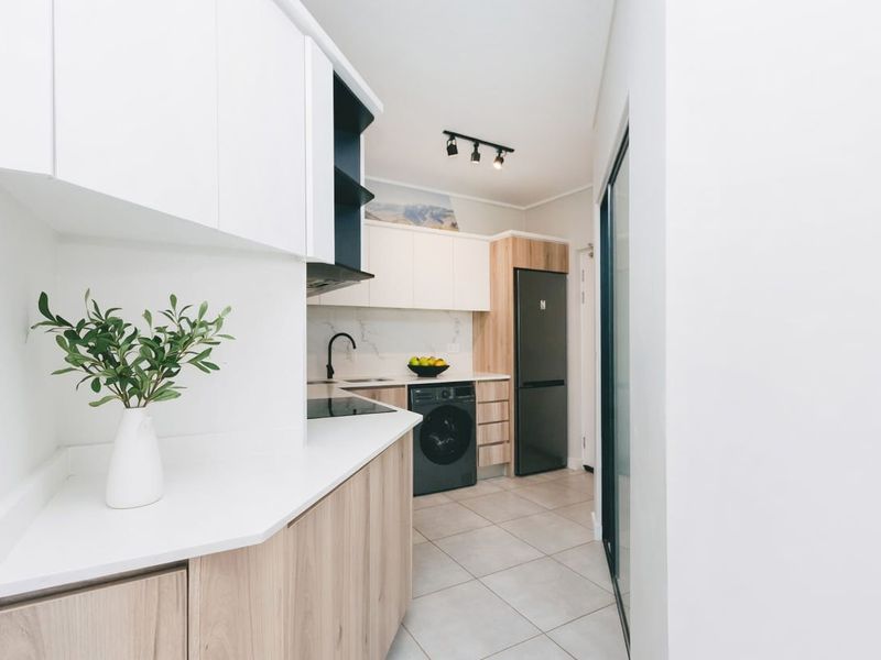 Modern kitchen featuring sleek white and wood-tone cabinetry, stone countertops, integrated appliances, and contemporary track lighting with neutral tiled flooring.