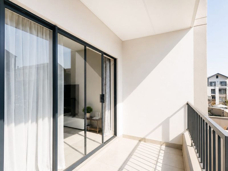 A modern, well-maintained balcony featuring tiled flooring, a sleek metal balustrade, and large sliding glass doors providing access to the interior living space.