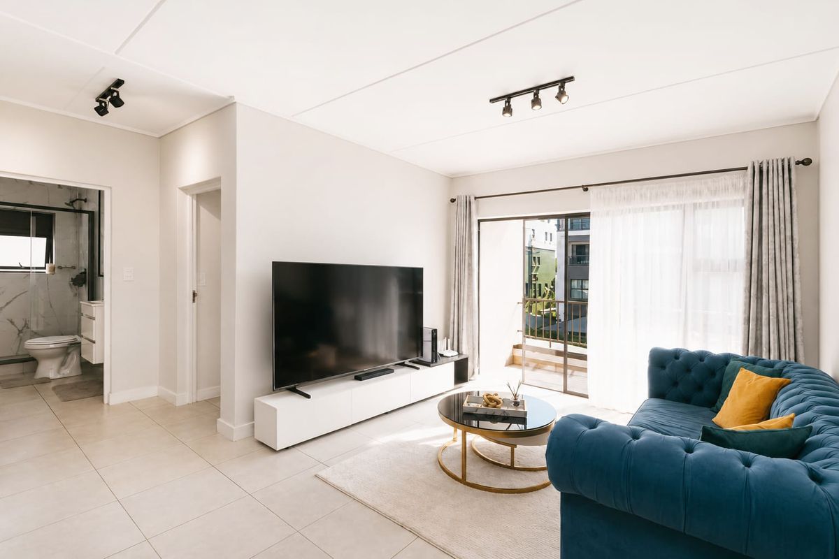Bright living room featuring tiled floors, modern track lighting, and a sliding glass door providing direct access to a private balcony.
