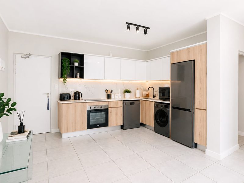 Modern kitchen featuring sleek white and wood-grain cabinetry, stone countertops, integrated appliances, and contemporary track lighting in a clean, open-plan layout.