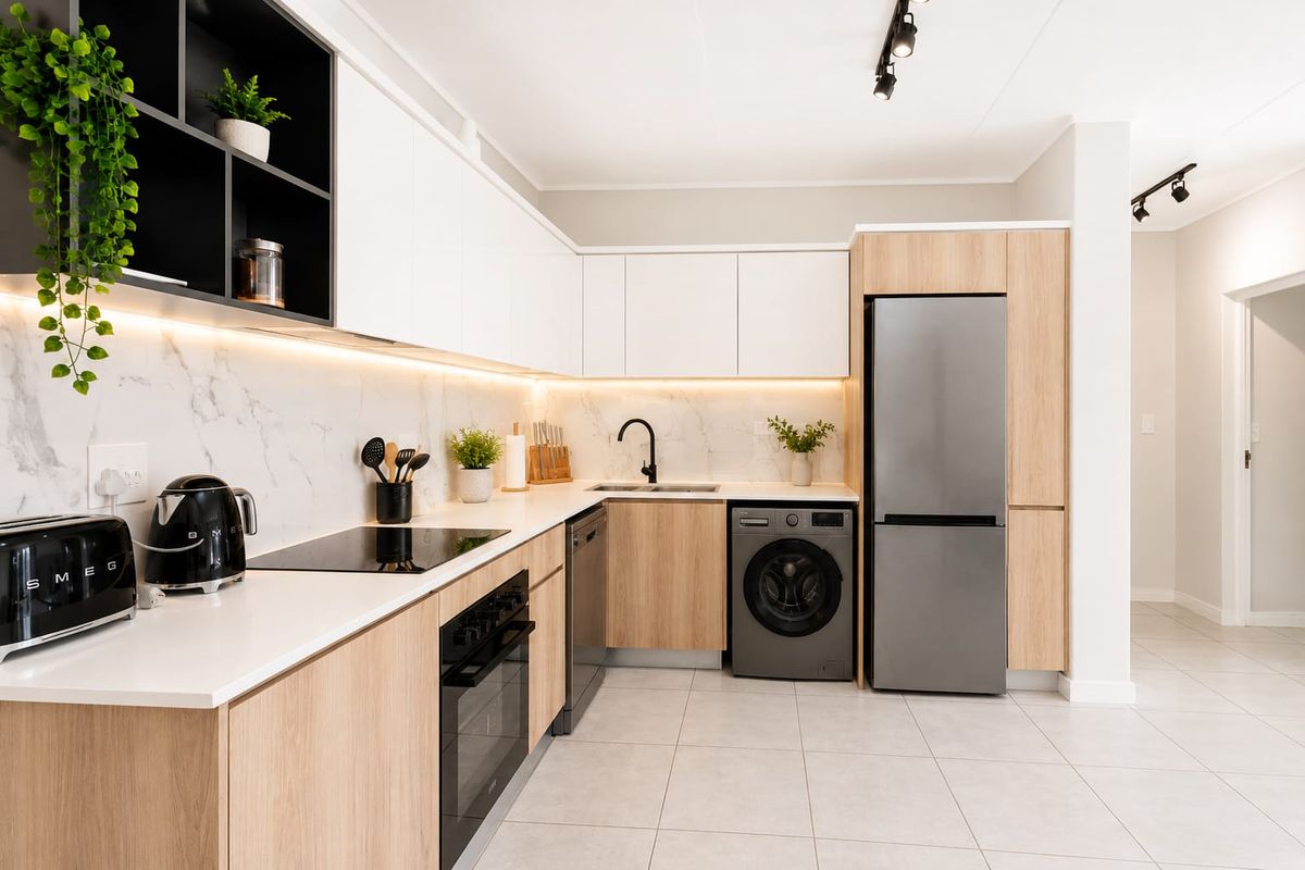 Modern kitchen featuring sleek white and wood-grain cabinetry, marble-look splashback, integrated appliances, and high-quality finishes with contemporary track lighting.