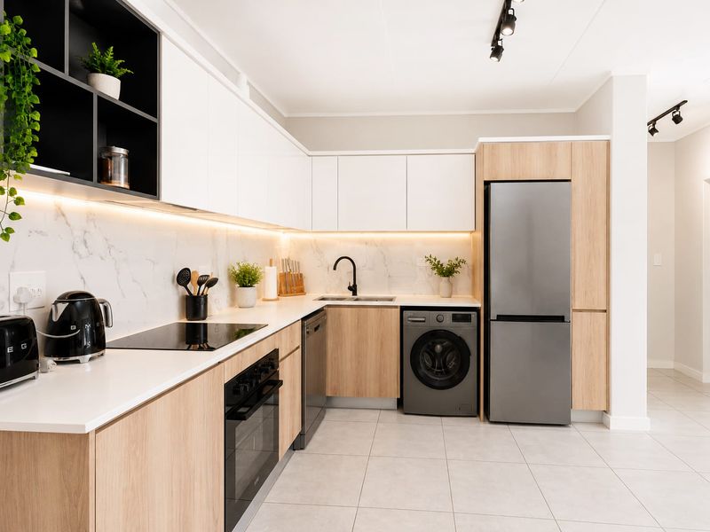 Modern kitchen featuring sleek white and wood-grain cabinetry, marble-look splashback, integrated appliances, and high-quality finishes with contemporary track lighting.