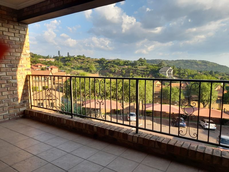 A covered balcony featuring a wrought iron balustrade and tiled flooring, offering elevated views over the complex and surrounding landscape.