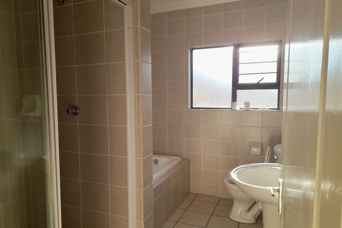 A functional bathroom featuring a shower enclosure, built-in bathtub, pedestal basin, and toilet with neutral wall and floor tiling.