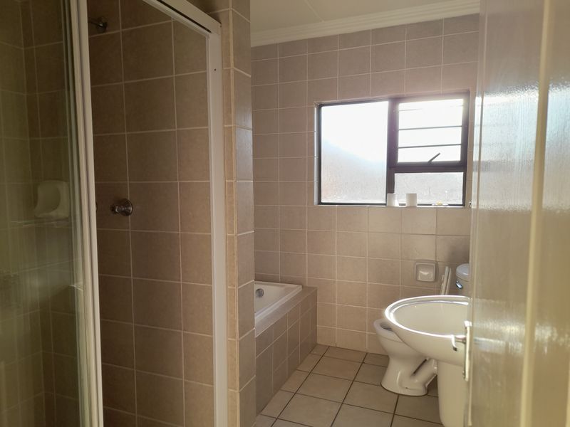 A functional bathroom featuring a shower enclosure, built-in bathtub, pedestal basin, and toilet with neutral wall and floor tiling.