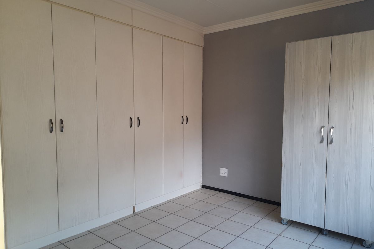 A bedroom featuring neutral tiled flooring, built-in cupboards, and a grey accent wall, providing a clean and functional space.